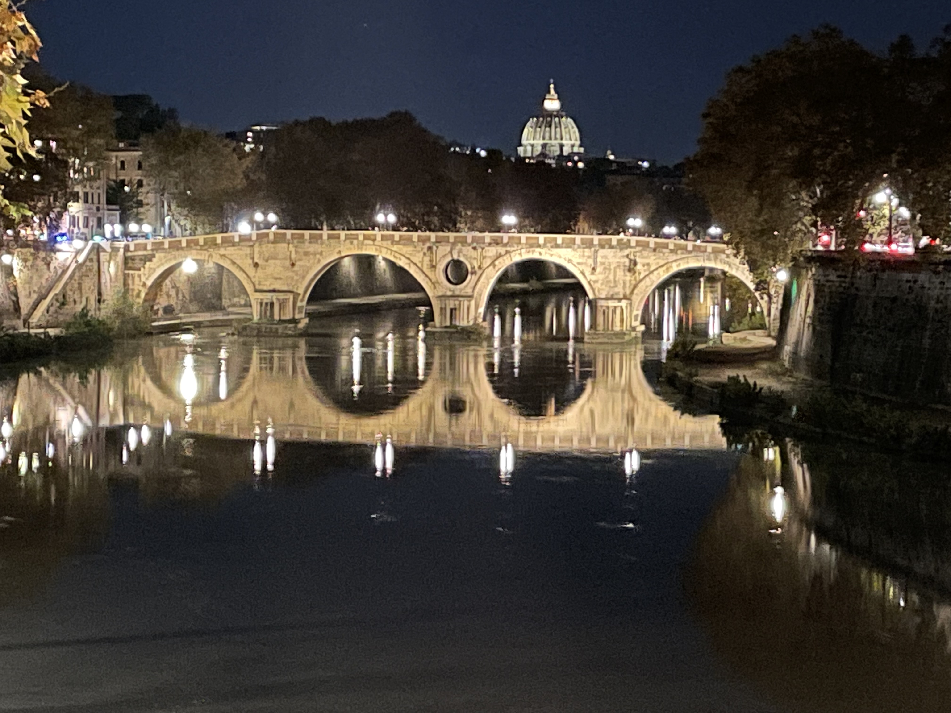 Looking down a river in Rome towards a bridge with lights at night